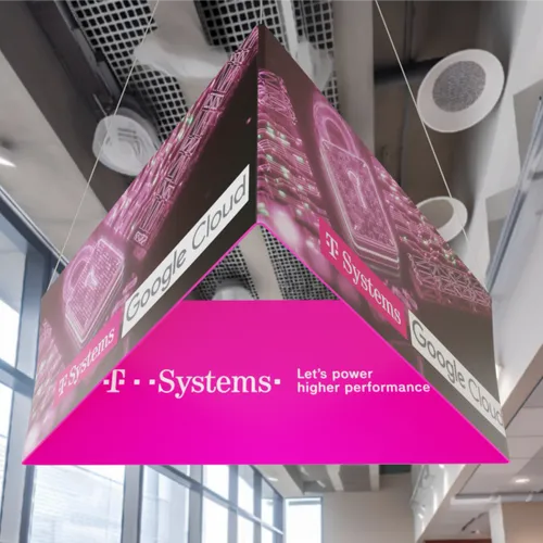 A hanging promotional display features branding for 'Google Cloud' and 'T-Systems' with the slogan 'Let's power higher performance'. It's suspended in a well-lit indoor space.